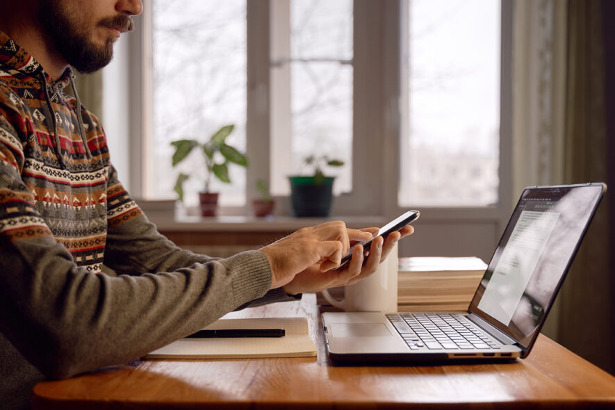 Man is sitting in front of his laptop, using his phone to book a builder