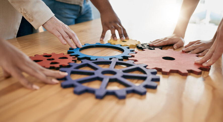 Hands, collaboration and gear with a business team working together in synergy for innovation at a workshop. Meeting, teamwork and creative with a man and woman employee group at work in the office